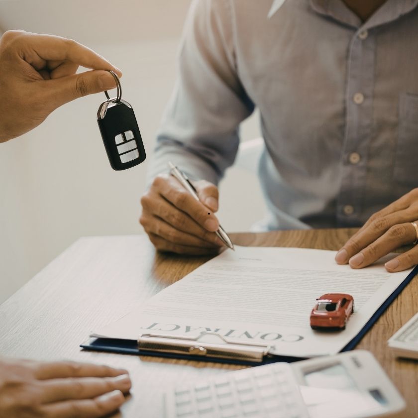 Car dealer handing keys to customer signing a contract at a dealership