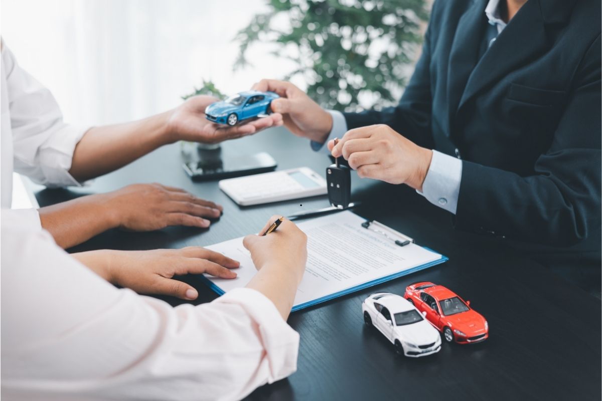 Car dealer signing paperwork with keys and toy cars on desk
